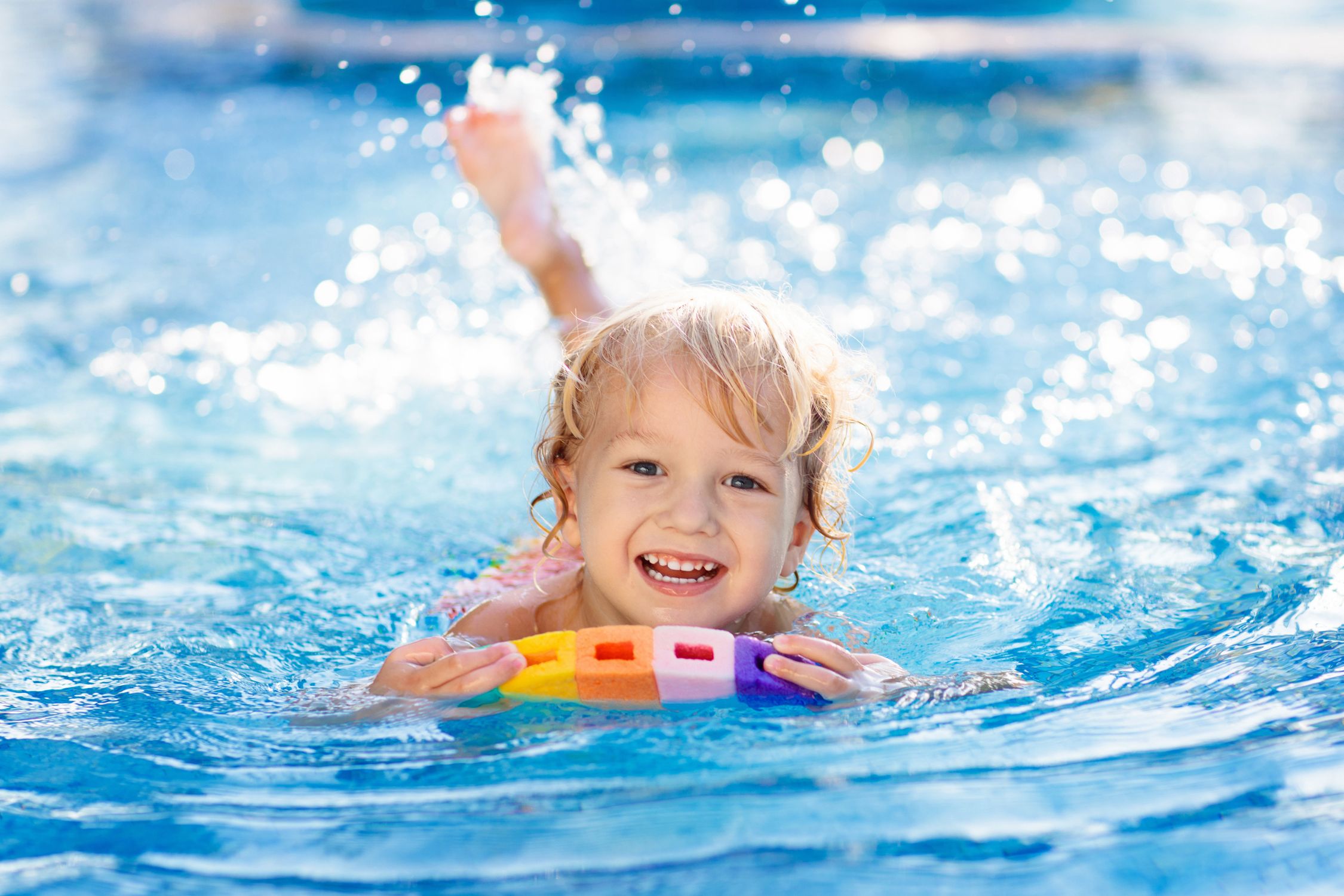 Blondes Kind mit Schwimmhilfe plantscht im Wasser