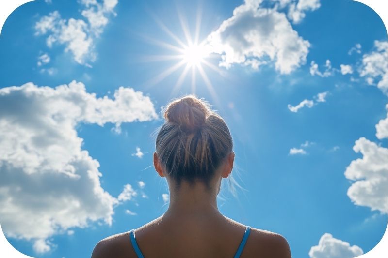 Frau steht mit dem Gesicht zur strahlenden Sonne