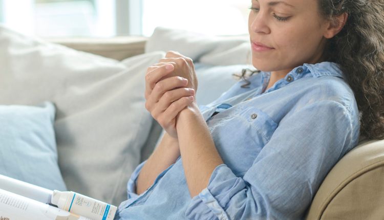 Frau sitzt auf einem Sofa und crent sich die Hände ein