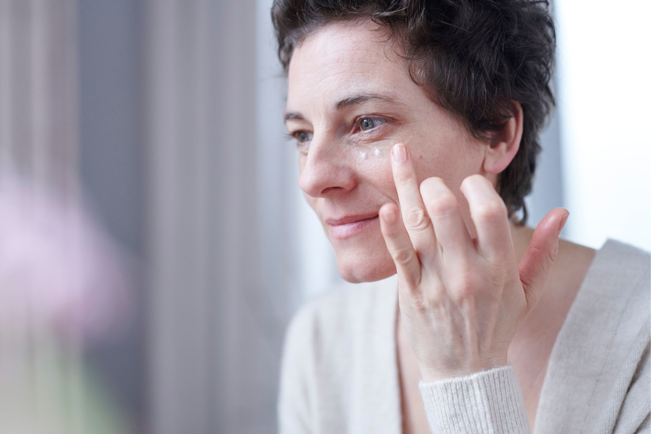 Eine Frau trägt eine Neurodermitis Augencreme punktweise unter dem Auge auf