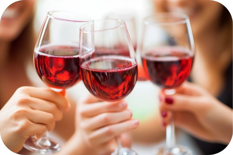Drei Hände halten drei Gläser Rotwein zum Anstoßen hoch