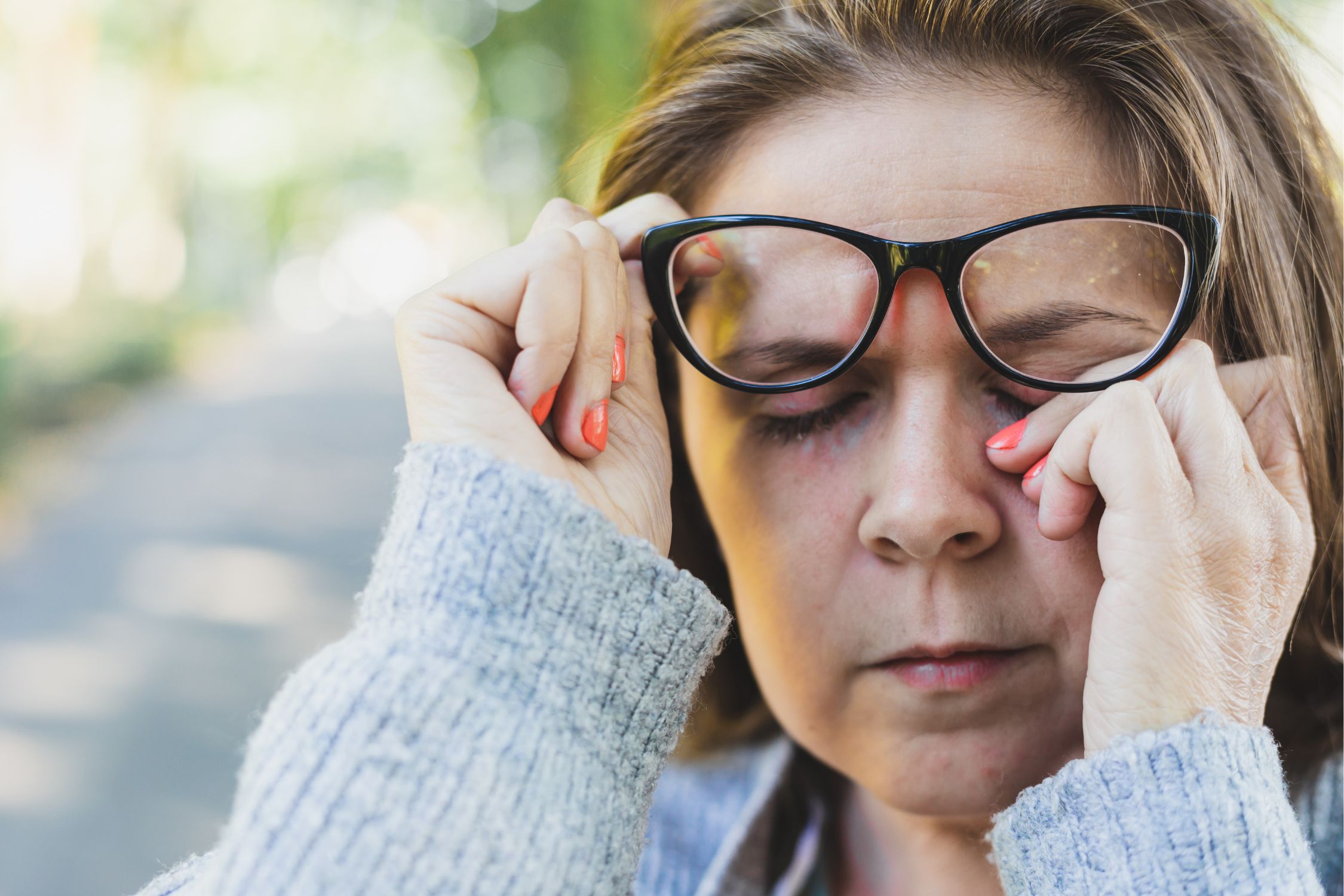 Frau mit Neurodermitis am Auge schiebt ihre Brille hoch und reibt sich die Augen