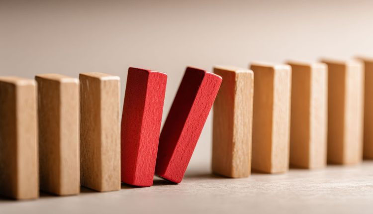 Dominoeffekt: Ein roter Holzklotz kippt und ist im Begriff, eine Reihe an holzfarbenen Klötzen umzustoßen
